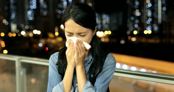 Woman suffer from sneezing in the city at night 