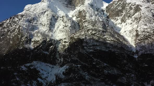 Aerial tilt up to reveal snow covered majestic mountain Fetanipa above UNESCO Naeroyfjord in Gudvang