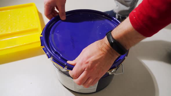 Male Hands Open the Lid of the Paint Bucket