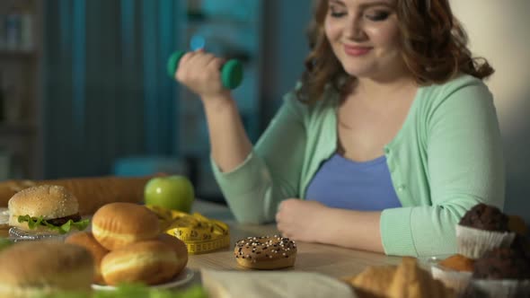 Overweight Girl Lifting Small Dumbbell and Looking at Donut With Smirk, Diet