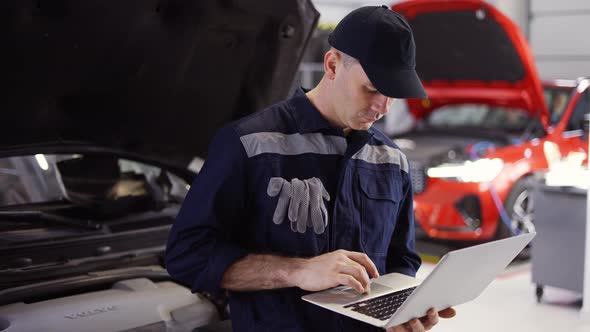 Car Mechanic Working on Laptop in Auto Repair Service Lean on a Car