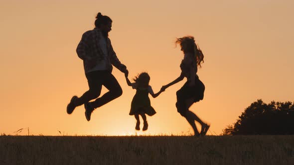 Three Silhouettes of People on Background of Sunset Sun Family with Small Child Daughter Jumping in