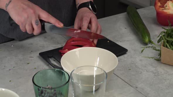 Tattooed chef slices fresh red bell pepper on countertop cutting board