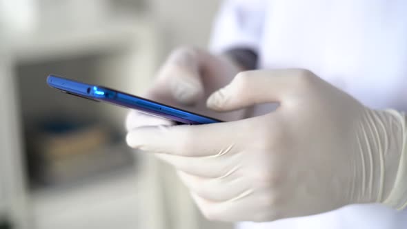 Hands of doctor in surgical gloves writing text message on smart phone