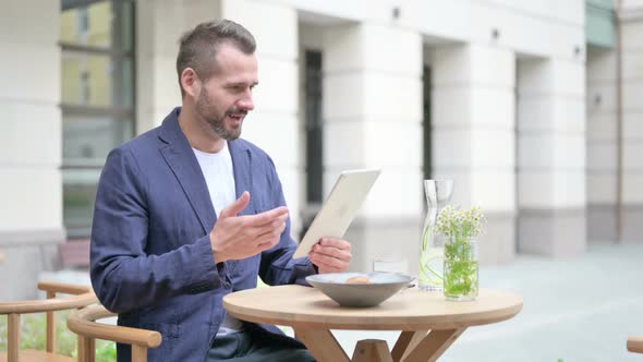 Man Celebrating Success on Tablet Sitting in Outdoor Cafe
