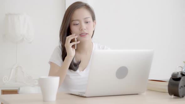 Young freelance asian woman smiling working laptop computer and talking customer with call phone.