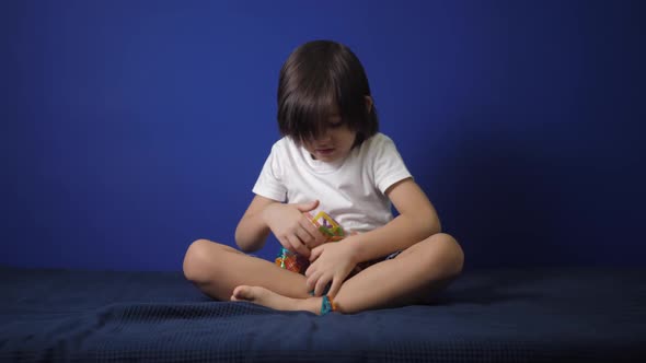 Boy Child in a White Tshirt Sits on a Bed Against a Blue Wall and Plays a Magnetic