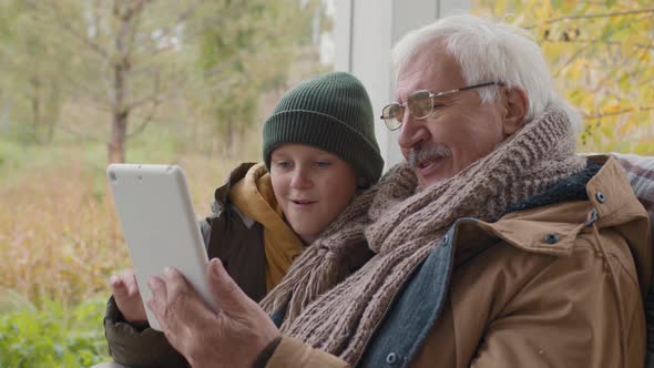 Child and Grandfather Sitting on Terrace and Using Tablet