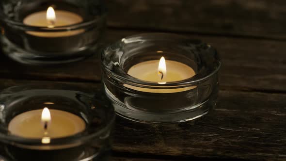 Tea candles with flaming wicks on a wooden background 