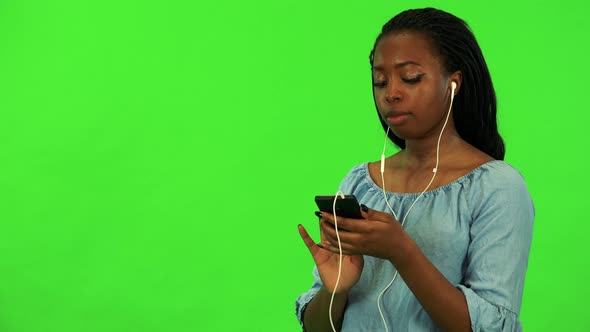 A Young Black Woman Listens To Music on a Smartphone - Green Screen Studio