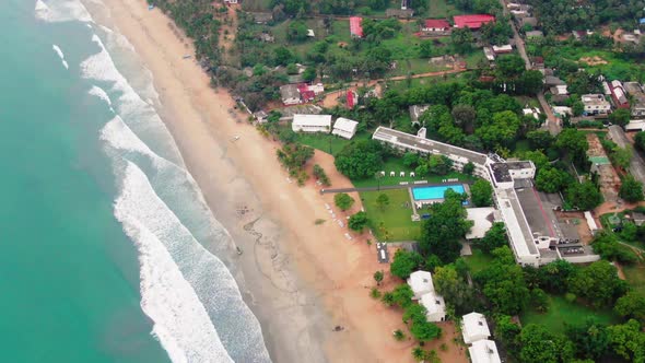 Aerial, tilt drone shot over waves and sand, on a paradise beach, towards buildings in Trincomalee c