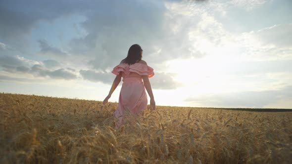 A Girl Walks Through a Golden Wheat Field at Sunset