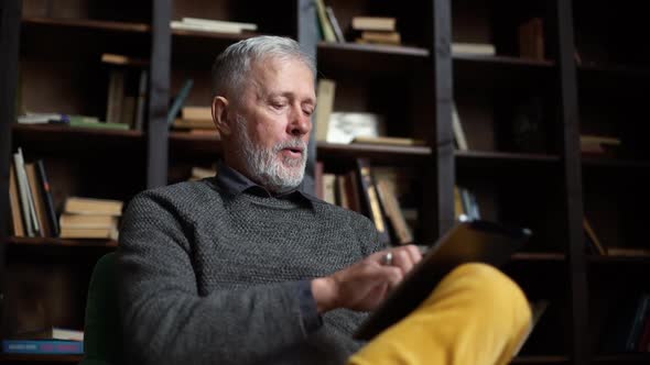 Closeup of Bearded Grayhaired Mature Adult Male Having Break with Digital Tablet Sitting at Home