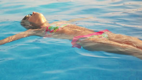 Girl in a Pink Swimsuit Swims on Her Back in a Pool with Clear Water on Summer Vacation