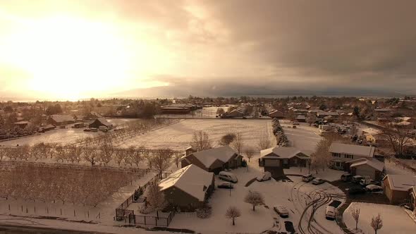 Aerial view over houses while snow is falling as the sun is setting.