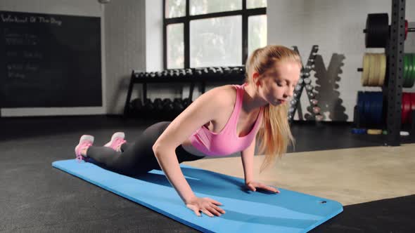 Young woman has workout at gym. Standing on knees and doing push ups with strong hands
