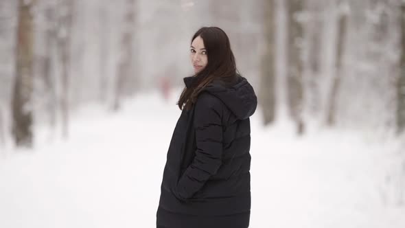 A Young Darkhaired Woman Walks Through a Snowcovered Forest Enjoying a Beautiful Winter Day