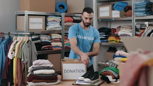 Caucasian Bearded Male Volunteer Sorting Shoes and Putting It Into the Cupboard Box at the Warehouse