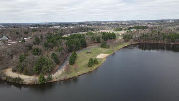 Aerial view off lake to park with woods, a shelter, open field, and a small empty beach.