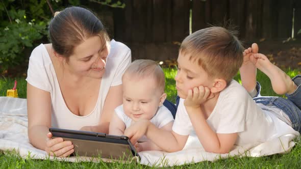 Happy Smiling Boy with Baby Brother and Mother Lying on Grass in Park and Browsing Internet on