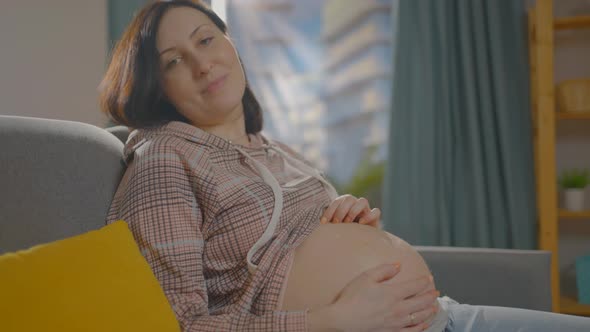 Pregnant Woman at Home Sitting on the Couch Daytime Looks at the Camera