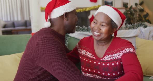 Happy senior african american couple wearing santa hats hugging in the living room
