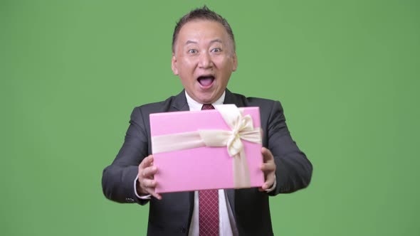 Mature Japanese Businessman with Gift Box Against Green Background