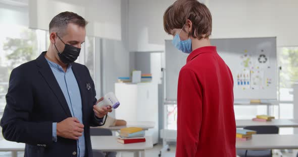 Portrait of Male Teacher Checking Temperature of Children Entering Classroom in School