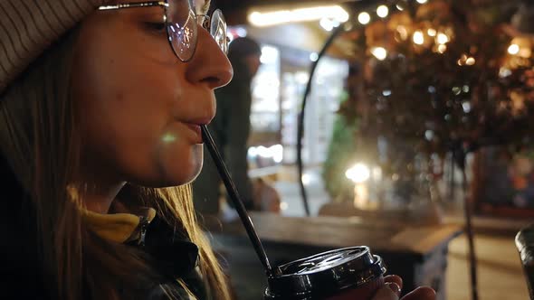 Portrait of a Young Woman Drinking a Hot Takeaway Drink on the Street of a Night City