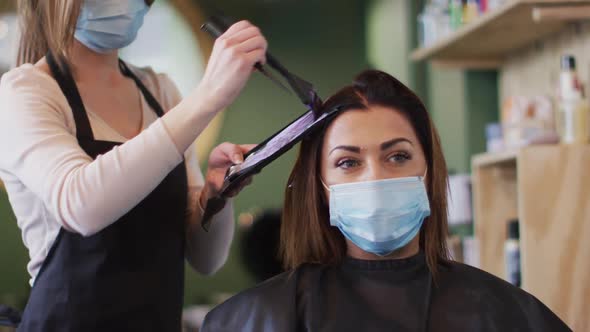 Female hairdresser dying hair of female customer wearing face mask at hair salon