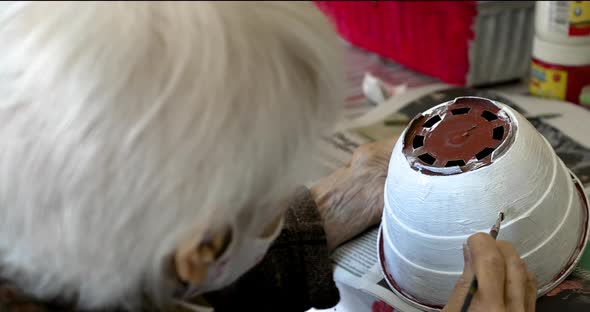 A tender grandma painting a flower pot as a hobby. Hand of an old woman holding a brush, close up