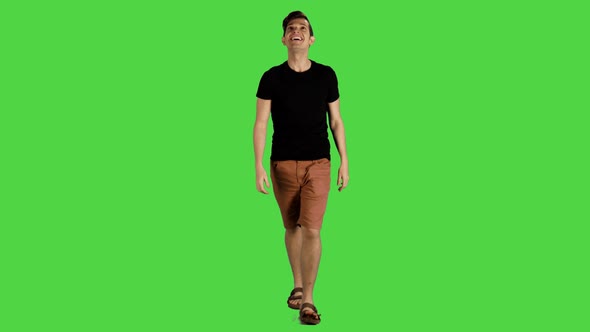 A young man smiling and looking around while walking over a green screen, 4k.