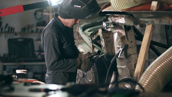 Male Worker at a Welding Factory is Examining Metal Construction to Weld Some Piece of Metal on It