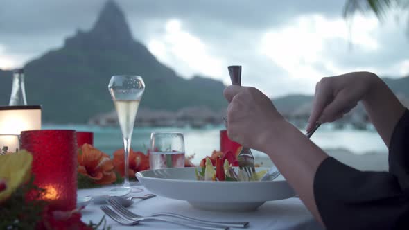 A man and woman couple dining on the beach of a tropical island resort at sunset in Bora Bora.