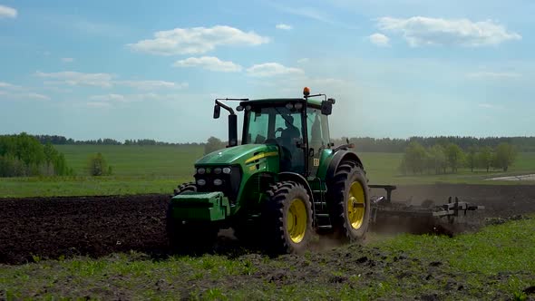 A rural tractor drags a plow across a field with rising dust