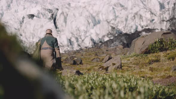 Traveller Carrying Guitar Case On Rocky Hill Next To Glacier