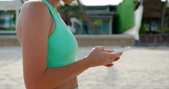 A Middle Shot of a Woman Walks on the Beach and Typing Text Message on the Smartphone