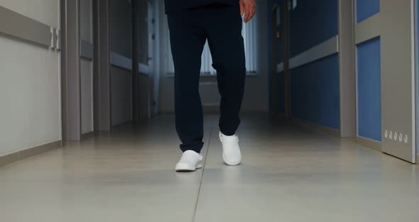 Mature Doctor Talking on a Mobile Phone While Walking Along Hospital Corridor