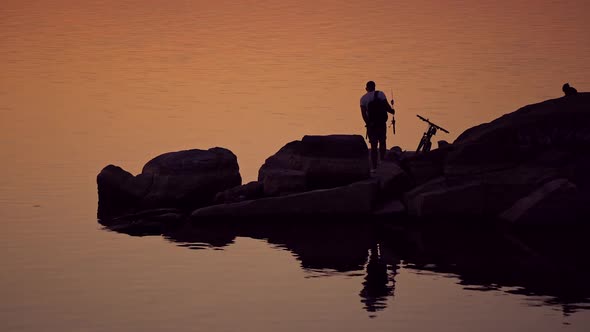 Man with fishing rods near his bike on the evening water background
