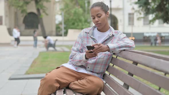 African Woman Using Smartphone While Sitting Outdoor on Bench