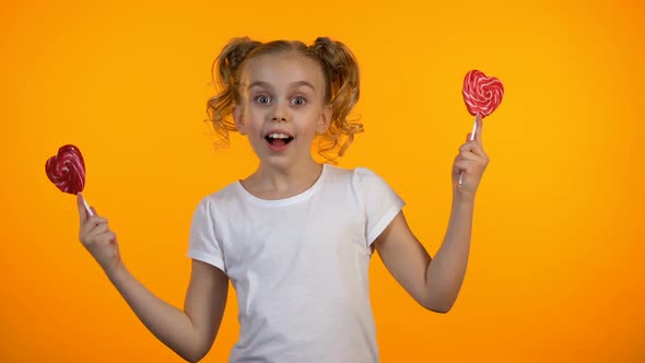 Adorable Girl Closing Eyes With Heart-Shaped Lollipops, Smiling and Having Fun