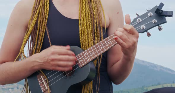 Close Up of Woman with Braids Playing Ukulele Outdoors