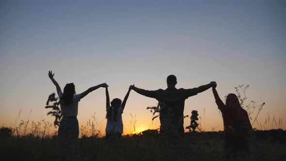 Mother and Father with Two Little Children Stand on Grass Field with Raising Hands at Sunset