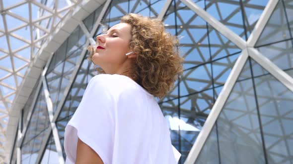 Young Female In White Dress Listening Music Using Wireless Bluetooth Earbuds