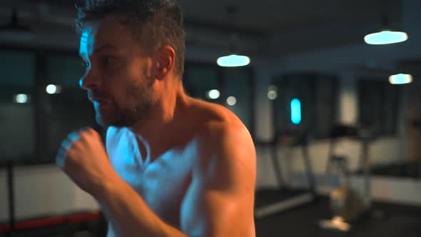 Alone Boxer is Working Out Blows on a Punching Bag in a Gym in Evening