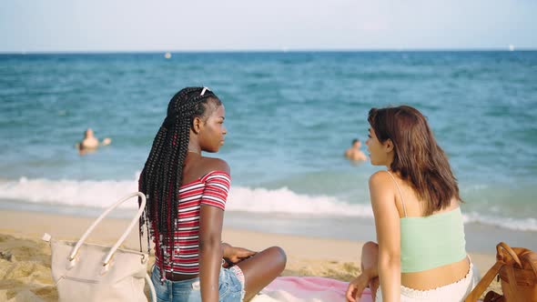 Two Multiracial Young Girls Sitting on Sandy Beach