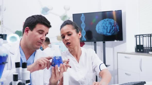 Team of Young Scientist Holding a Smoking Blue Liquid in a Recipient