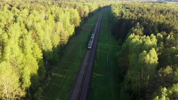 Aerial drone view of a modern electric passenger train passing through a beautiful forest
