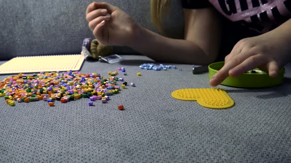 Child making art with perler beads,on the sofa.