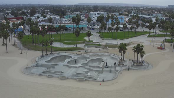 AERIAL: Turn Around Venice Beach Skatepark with Bikers and Palm Trees in Morning, Cloudy Los Angeles